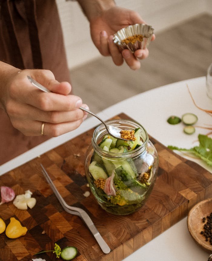 Hands carefully preparing pickled vegetables with cucumbers and garlic in a kitchen setting.